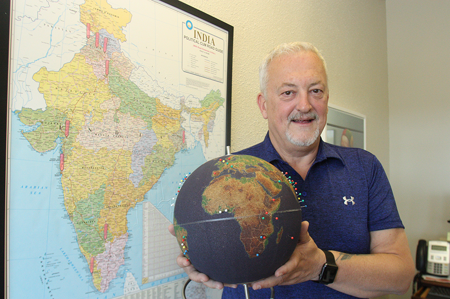 Photo of older man with grey hair holding a globe with colourful pins in it.