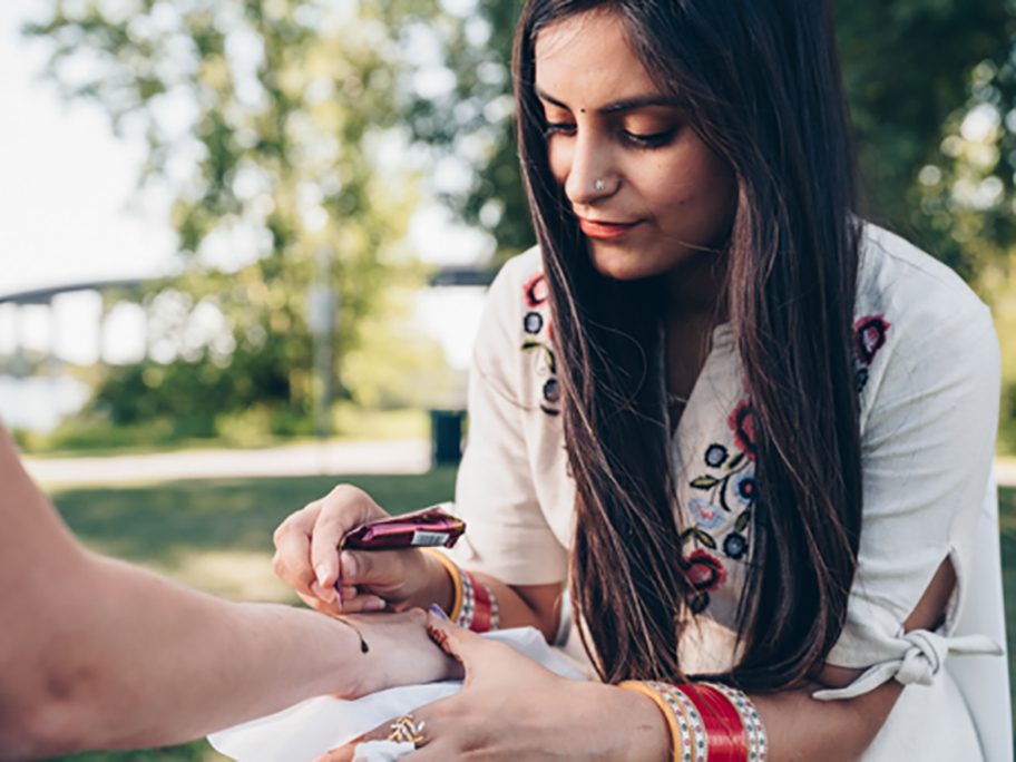 A young Indian woman applying a henna tattoo in a park