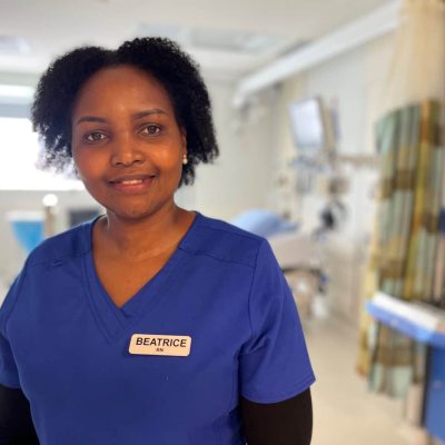 A photo of a person in blue scrubs with a nametag that says BEATRICE RN standing in a hospital room.